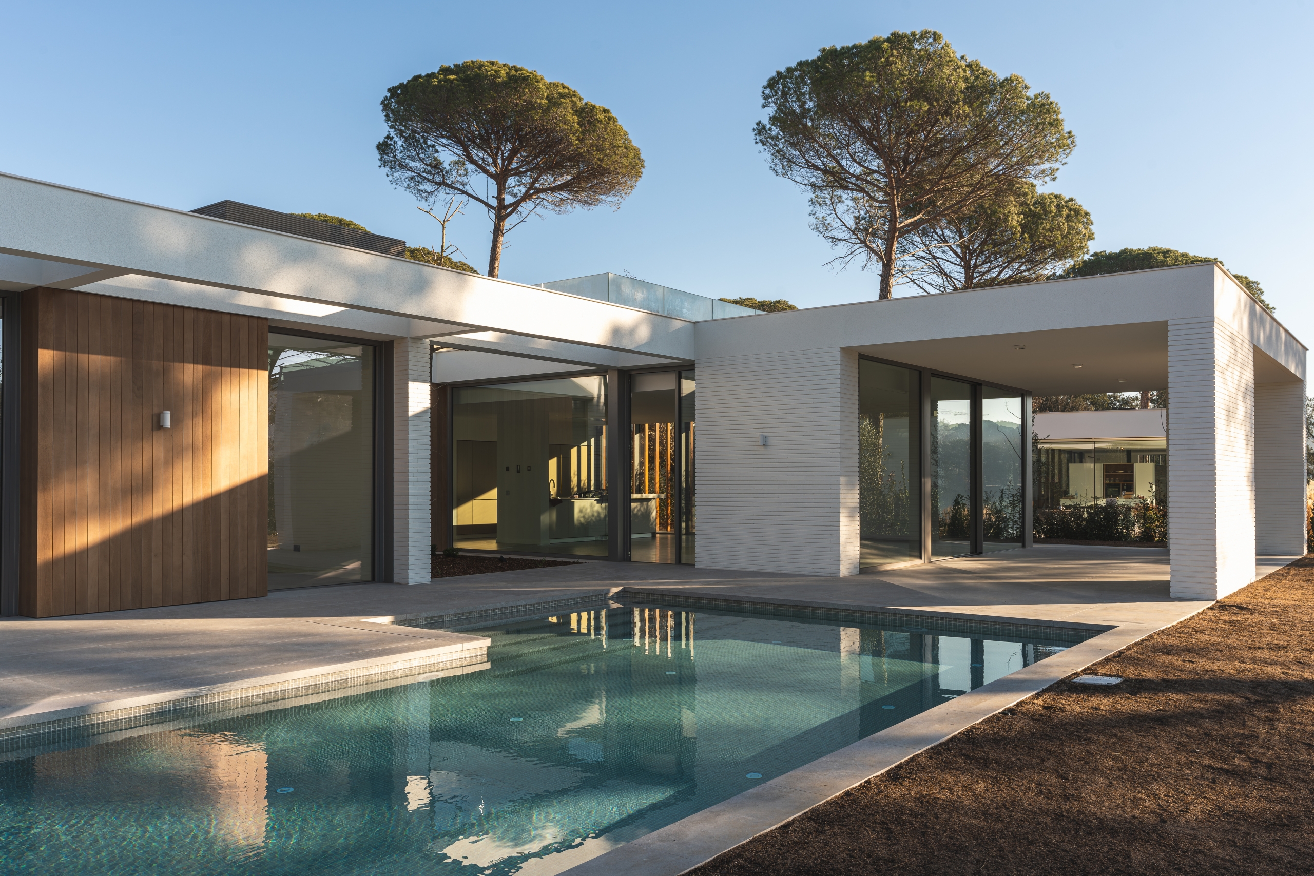 Outdoor view of a white and wooden luxury house with swimming pools and pine trees outside Construcción de Proyectos Inmobiliarios Residenciales Guatemala